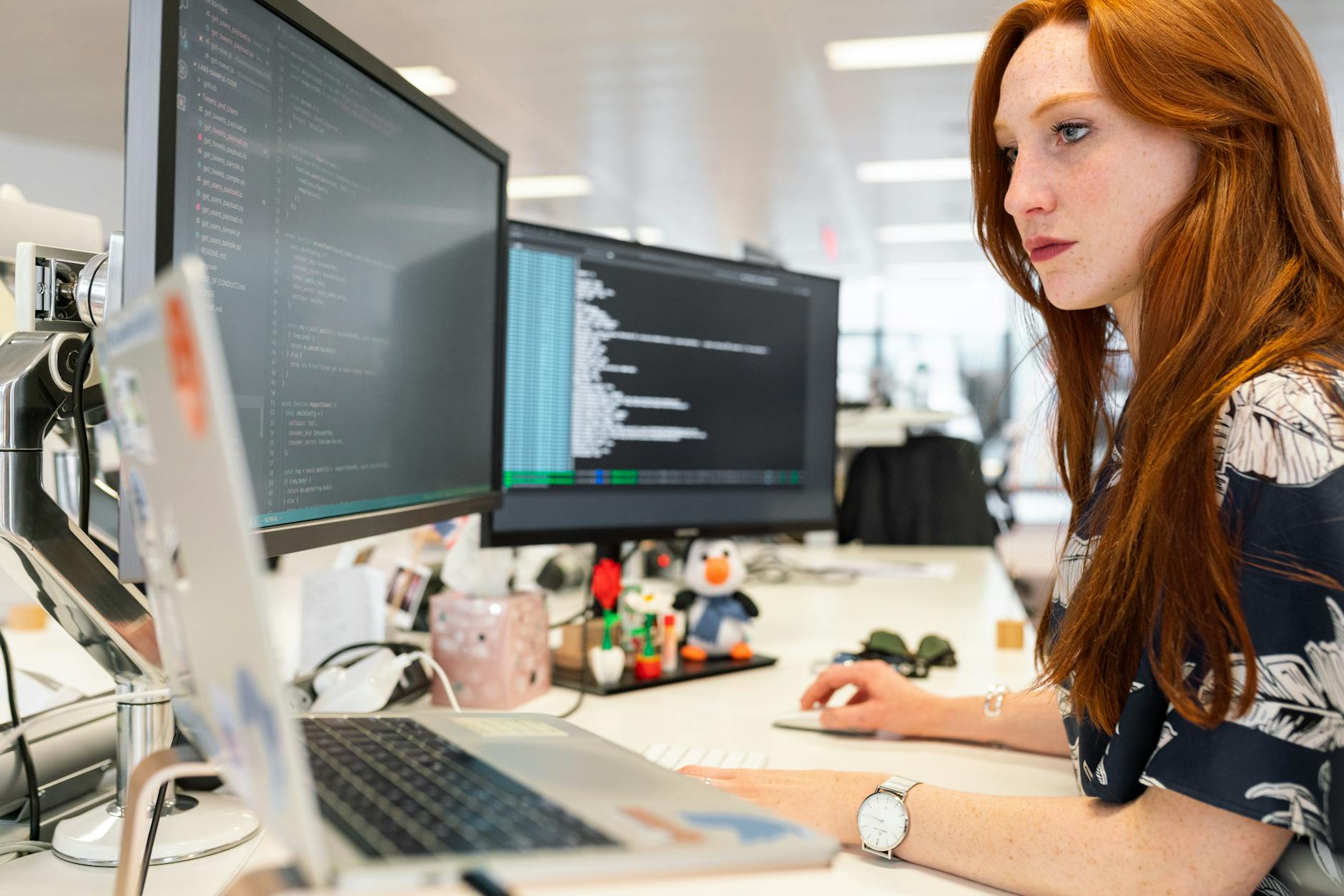 Programistka przy dwóch monitorach pracuje nad kodem w biurze IT